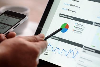 laptop with social media analytics on it, hand holding a pen and pointing to graph
