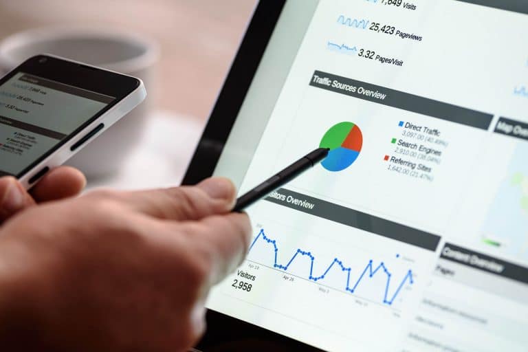 laptop with social media analytics on it, hand holding a pen and pointing to graph